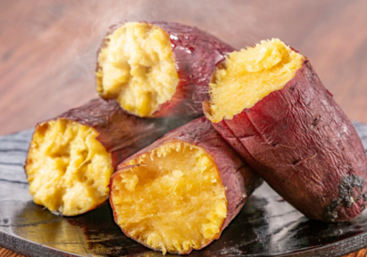 Steaming roasted sweet potatoes with golden, fluffy interiors and reddish-brown skins, served on a dark wooden plate.