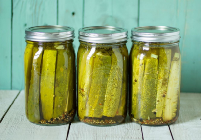 Three mason jars filled with pickle spears and brine, sitting on a white wooden surface with a teal wooden background.