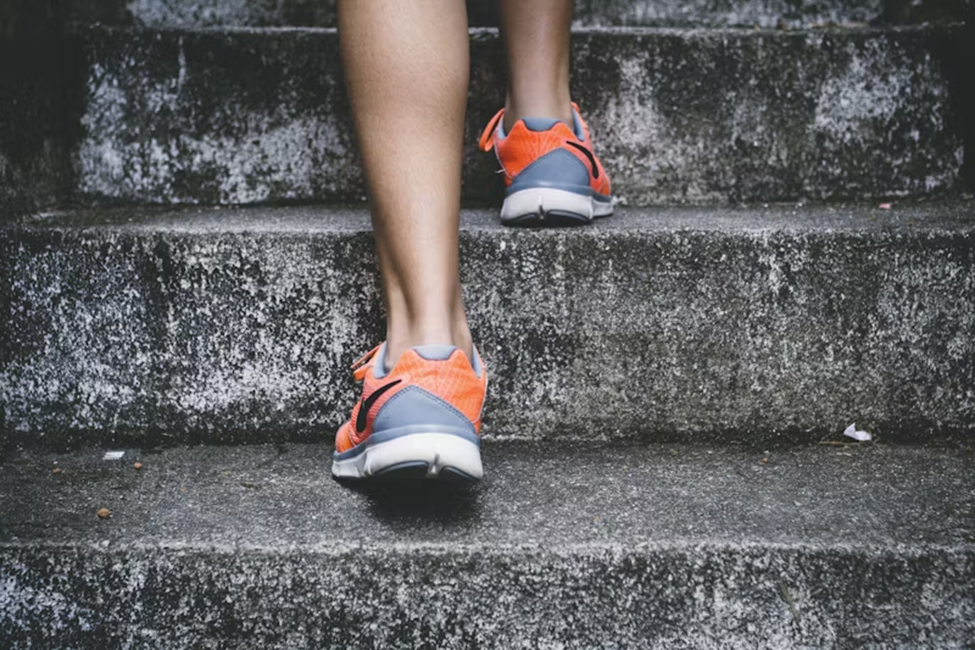 A person wearing orange and gray sneakers climbing up concrete stairs, with the focus on their legs and shoes.