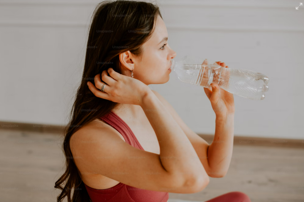 A young woman in activewear drinking water, emphasizing the importance of hydration weight loss routines.