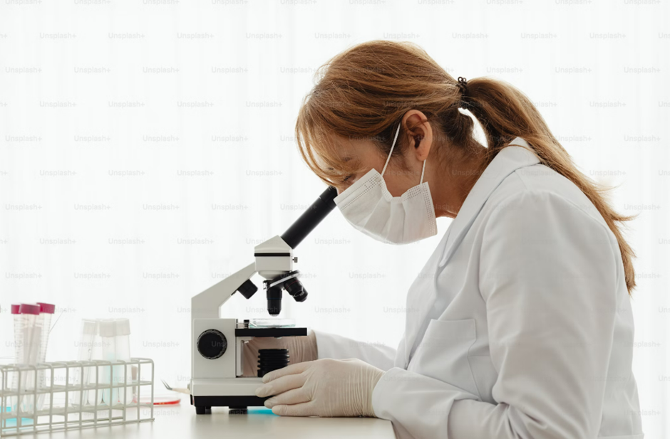 A scientist wearing a mask and lab coat using a microscope, surrounded by test tubes and laboratory equipment, symbolizing research and scientific study on diets and health.