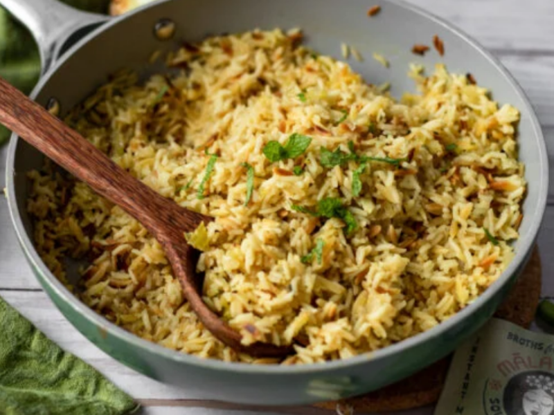 A skillet filled with flavorful cooked rice garnished with fresh mint, accompanied by a wooden spoon for serving.