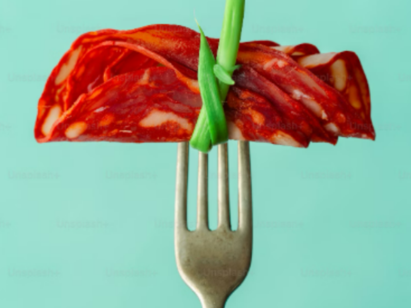 Close-up of a fork with thin slices of cured meat and a green bean garnish, illustrating a balanced meal choice for incorporating proteins and vegetables into salads.